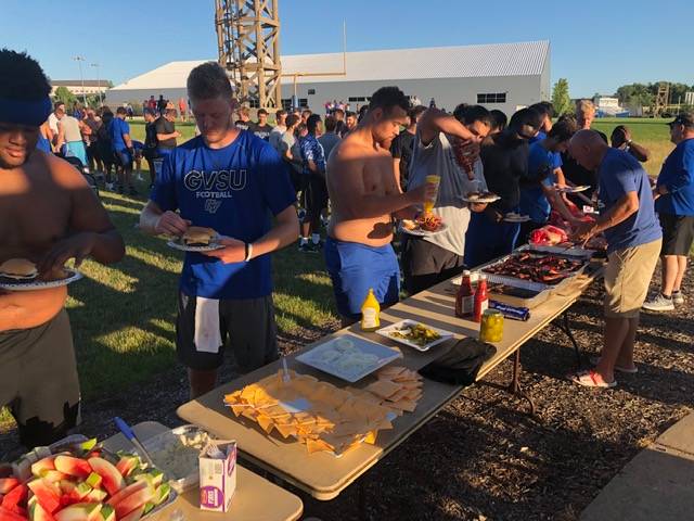 a line of football players waiting to be served food by the alumni